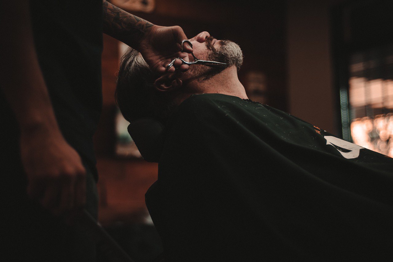 homem sentado na cadeira da barbearia cortando a barba
